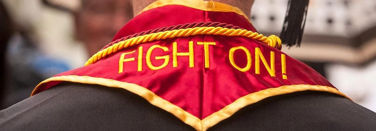 man is seen from behind with the words 'Fight On!' across his graduation sash