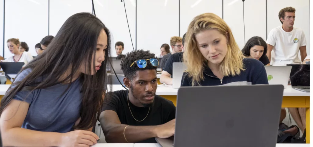 three students of different ethnic backgrounds work together on a laptop computer