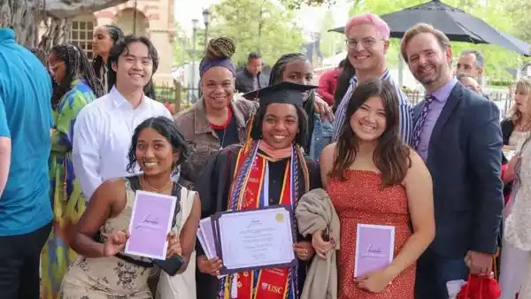 a group of friends surround a recent USC graduate holding up her diploma