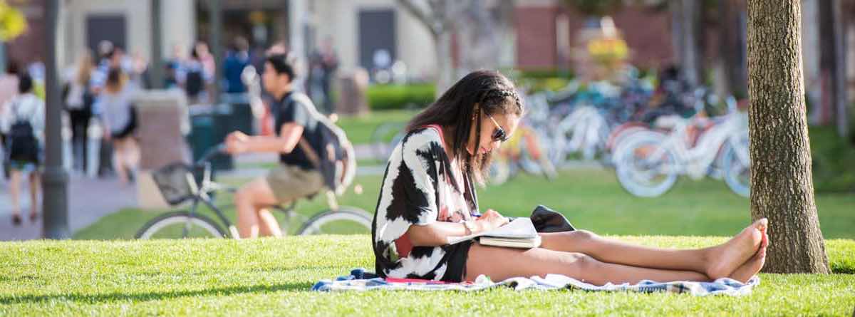 girl sits on a campus lawn reading a book