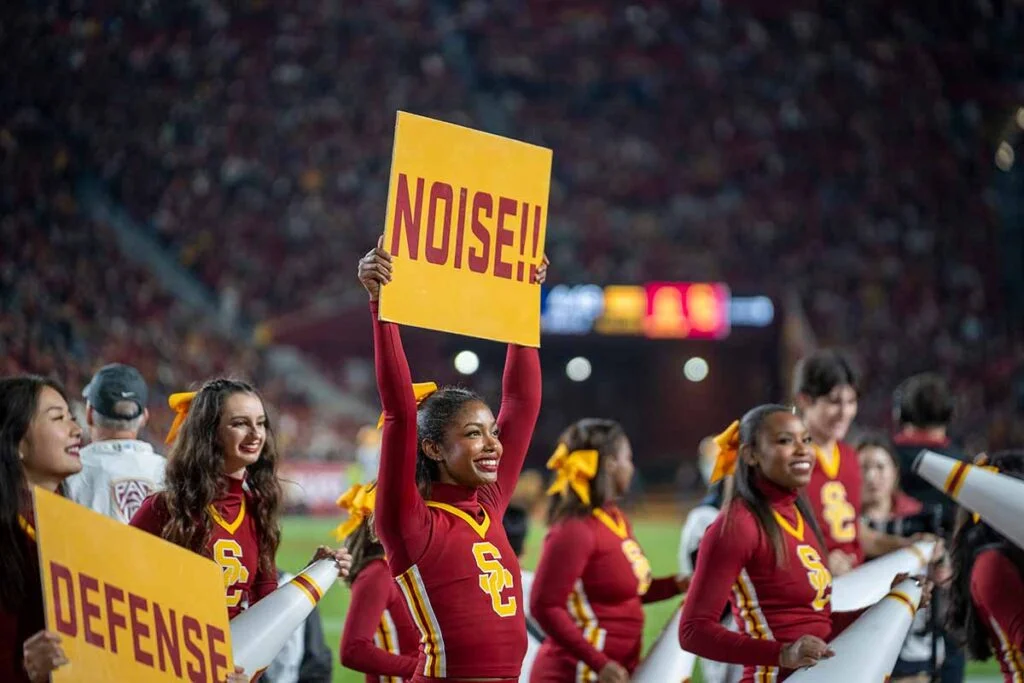 woman in cheerleading outfit holds up a sign with the word noise