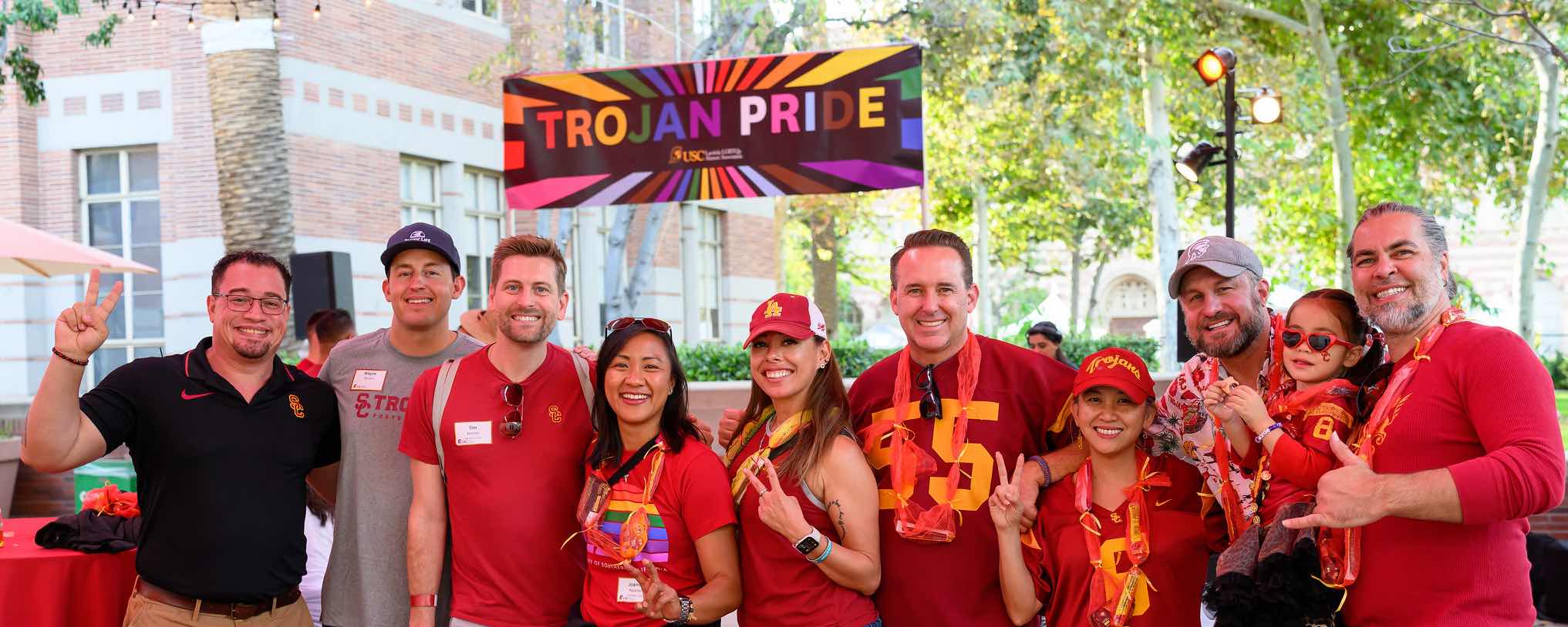 group posing in front of a Trojan Pride rainbow sign