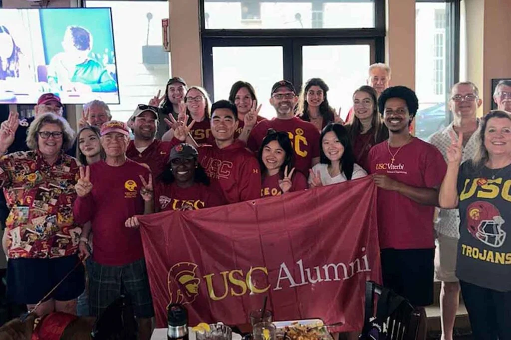 a group holds up a USC Alumni flag at a watch party